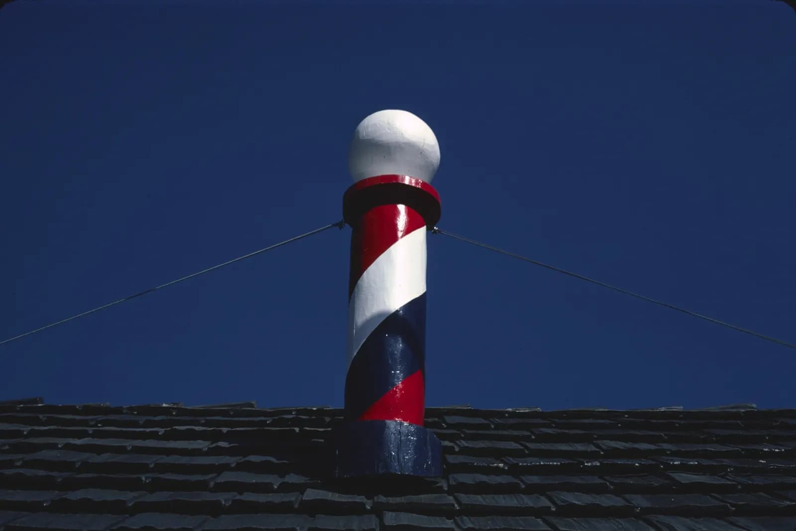 Un palo del barbiere bianco, rosso e blu sul colmo di un tetto, contro il cielo.