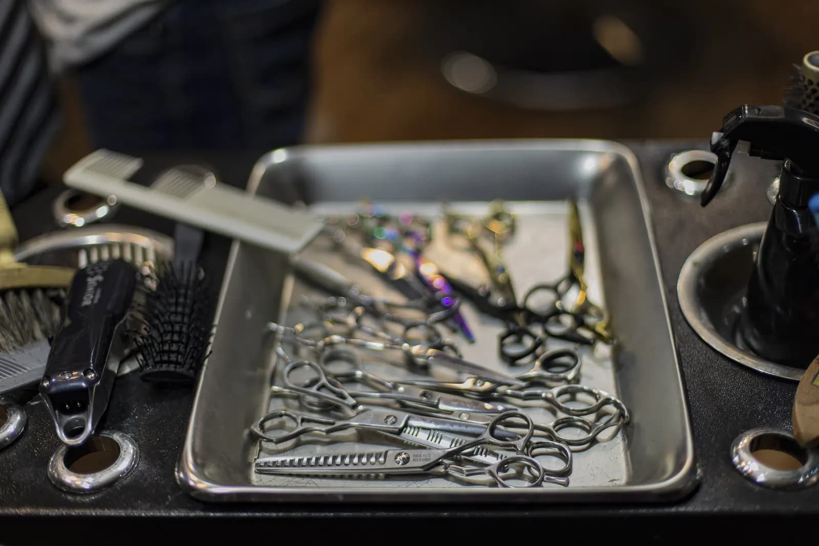 Il piano di lavoro di una barberia: vassoio di forbici, spazzole tonde, spruzzino e rasoio elettrico.