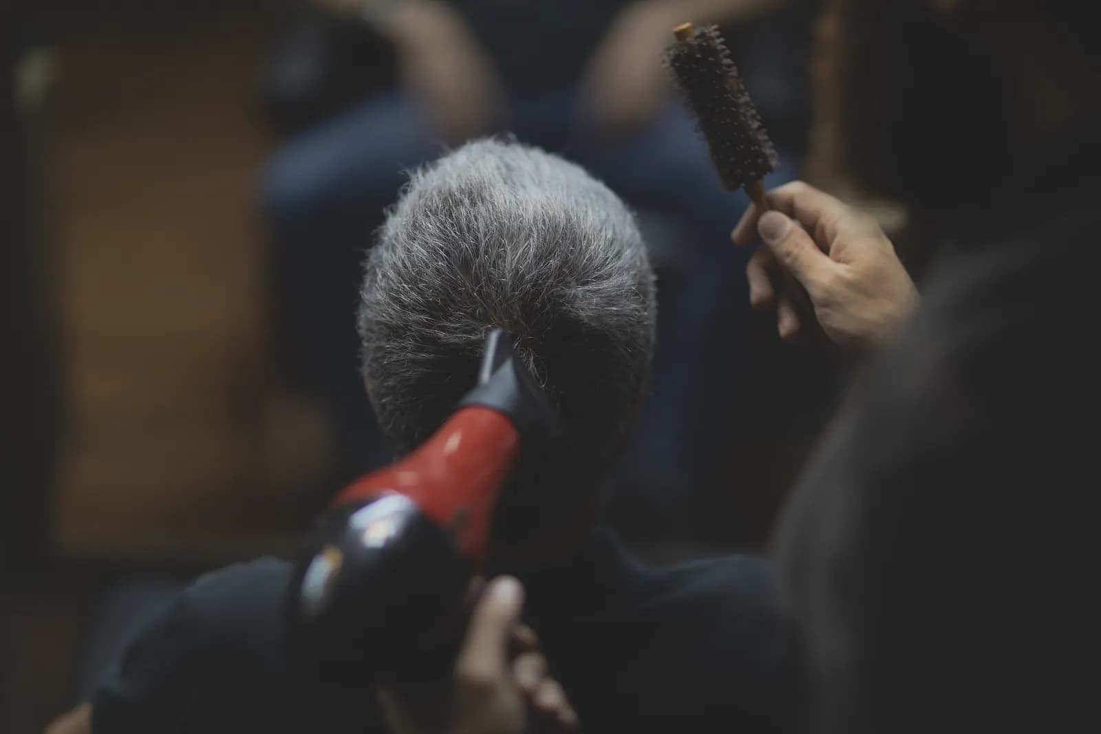 Phon e spazzola tonda su capelli brizzolati, ripresi da dietro.